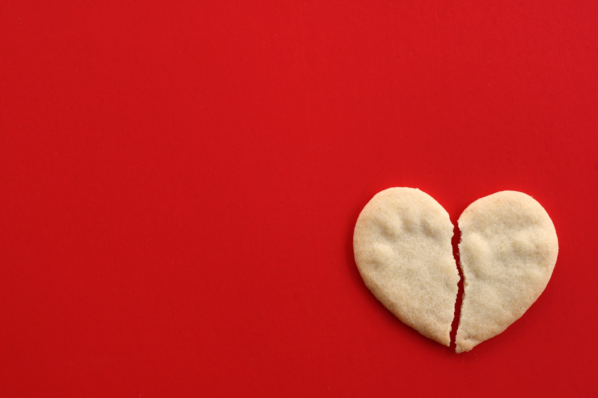 Broken heart cookie on red - concept breaking up, divorce, ending relationship, brokenhearted