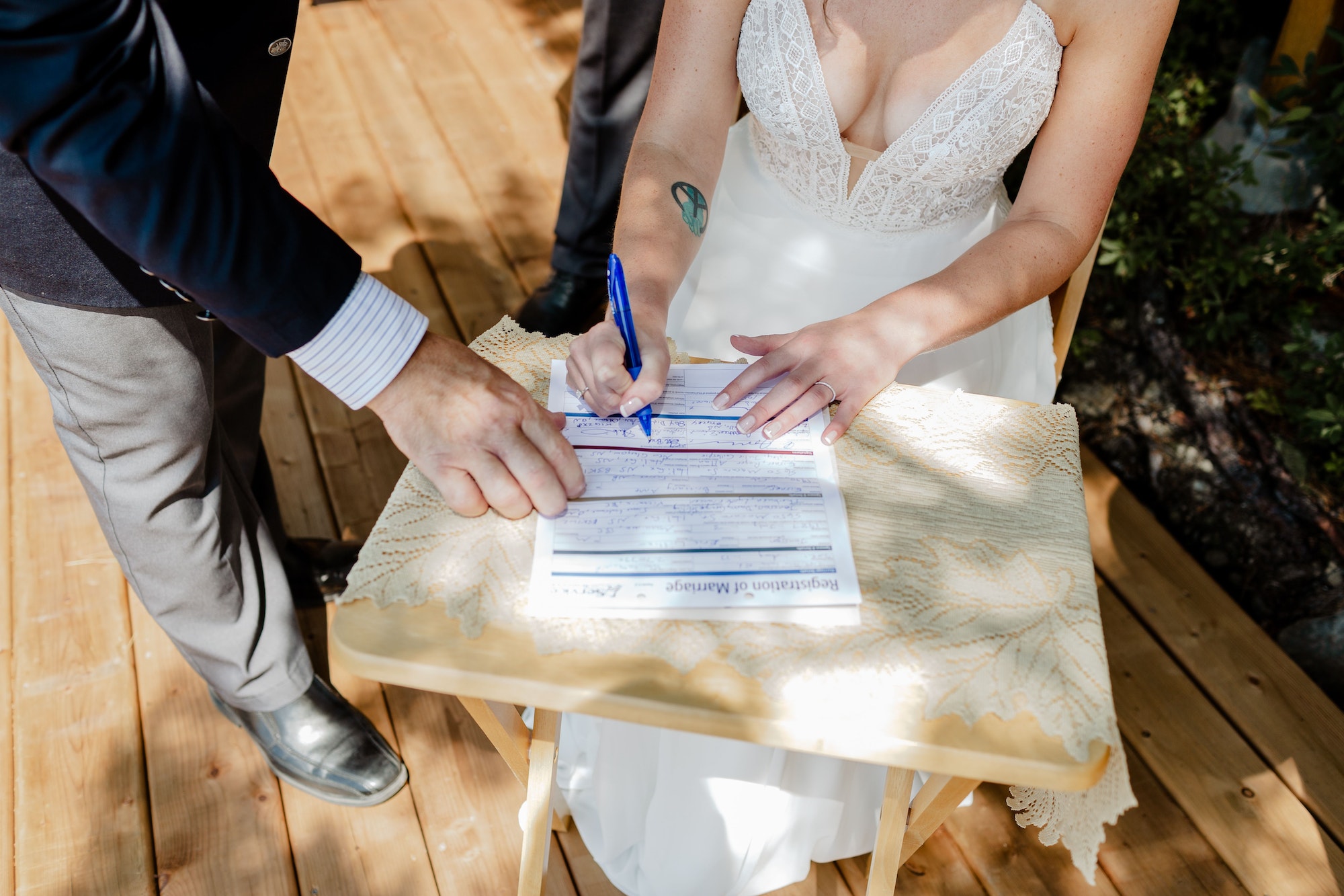 Closeup shot of a bride signing a wedding contract papers on a wooden table on a sunny day