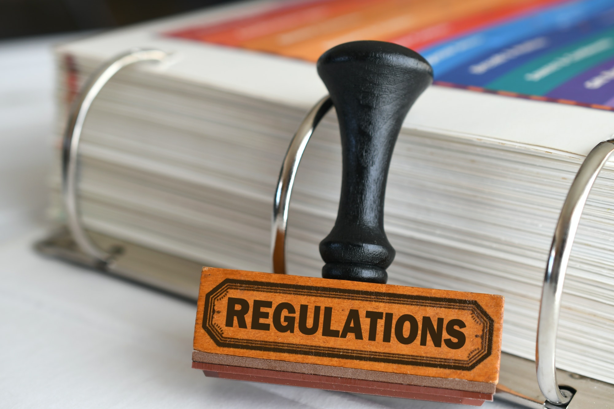 Regulations rubber stamp next to handbook of rules, compliance concept