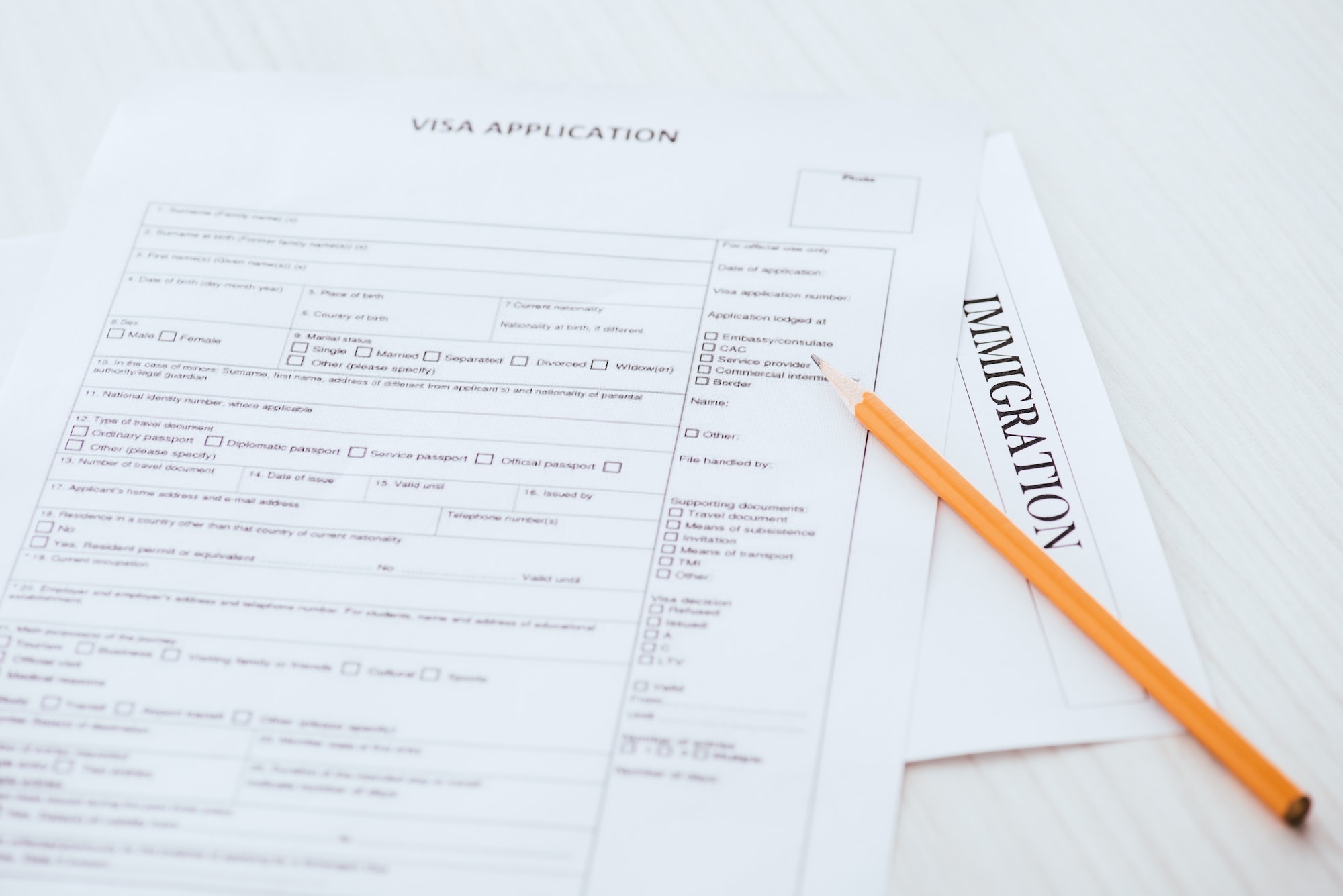 selective focus of wooden pencil near document with visa application and immigration lettering